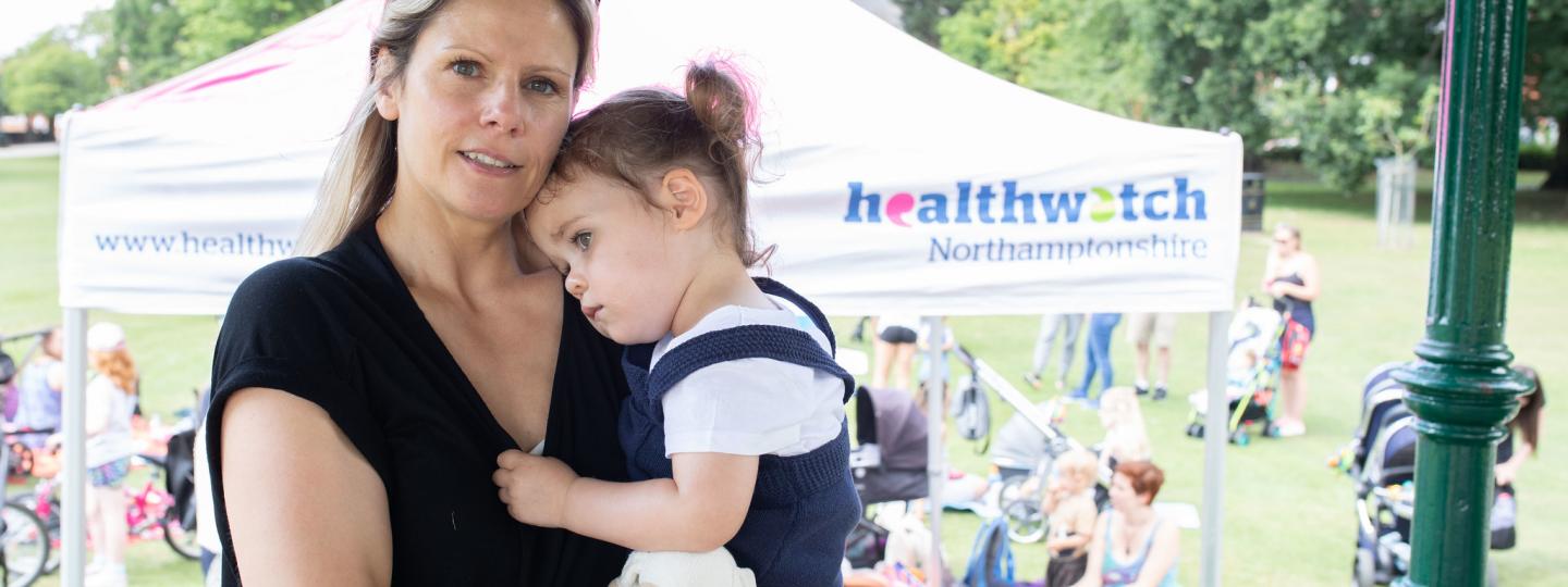 Mother holding her daughter on her hip at a Healthwatch event 